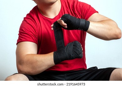 Close up man torso in red sportswear, bandaging his hands with boxing bandages, sitting. Moment before match or training. Copy space. - Powered by Shutterstock