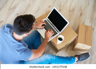Close up of man using a laptop next to moving boxes 