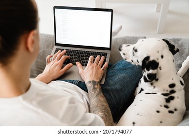 Close Up Of A Man Using Laptop On His Lap While Sitting With His Dog On A Couch At Home