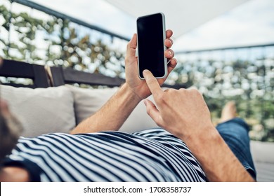 Close up of man using smartphone while lounging on apartment terrace