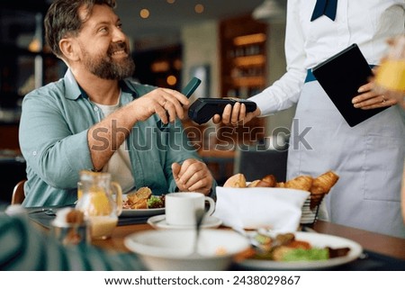 Close up of man using smartphone while paying to a waitress in a restaurant.