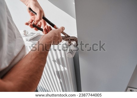 Close up of man using wrench tool while installing heating radiator in apartment under renovation. Male plumber working on heating system installation. Home renovation and plumbing works concept.
