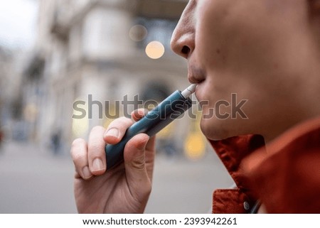 Close up of a man vaping with electronic cigarette outdoor on street. Attractive handsome male tourist travel alone on street, enjoy blowing the dense smoke out during walking in city town for holiday