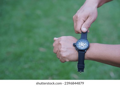 Close up man is wearing black leather hand watch, outdoor background. Concept, ashionable accessory for time telling, make you look stylish, punctual and smart. Analog wrist watch.                    