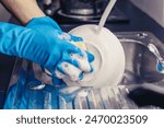 Close up of a man wearing a blue rubber glove was washing the cup with a dish washing liquid in the sink in the kitchen.