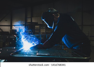 Close up of a man welding in a dark factory that causes sparks and light. - Powered by Shutterstock