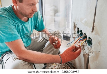 Close up of man in work gloves sitting by the wall and putting electrical wire cable in bottle with liquid. Male electrician installing electrical wiring in apartment under renovation.