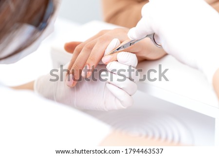 Close up of manicurist using manicure scissors to remove cuticle of female nails in manicure salon