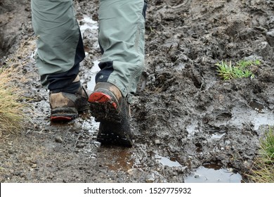 Close Up Of Man's Boots And Bottom Half Of Legs Hiking Through Mud