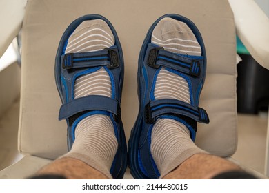 Close Up Of A Man's Feet On A Plastic Chair Wearing Beige Socks With White Stripes And Sandals.