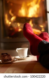 Close Up Of Mans Feet Relaxing By Cosy Log Fire With Tea And Cake