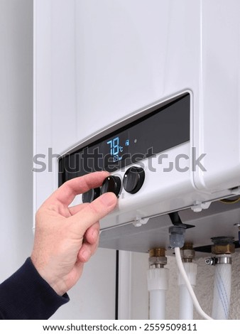 Close up of a man's hand changing the temperature on a modern digital gas boiler. Setting the central heating level on a gas boiler panel. Vertical image.