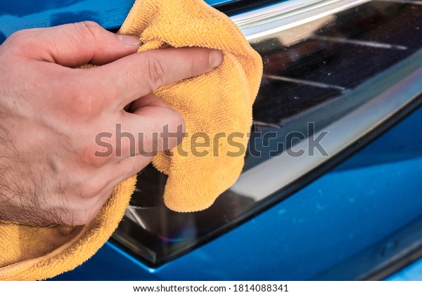 Close up mans\
hand cleaning or polishing a headlight of a blue automobile with a\
microfiber rag. Car washing\
concept.