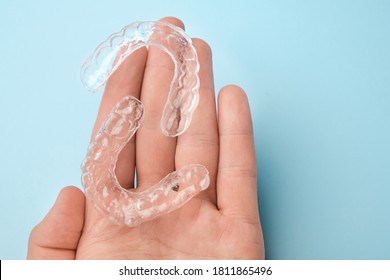 Close up mans hand holding invisible aligners for whitening and straightening of teeth on the blue background. Orthodontic therapy after brackets. Teeth healthcare