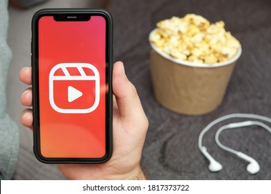 Close Up Mans Hand Holding A Mobile Phone With Instagram Reels Logo With Apple Earphones And Popcorn Box Next To Him, August 2020, San Francisco, USA