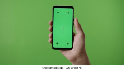 Close up of man's hand holding a smart phone with vertical green mock up chroma key screen and doing gestures on touchscreen  - Powered by Shutterstock