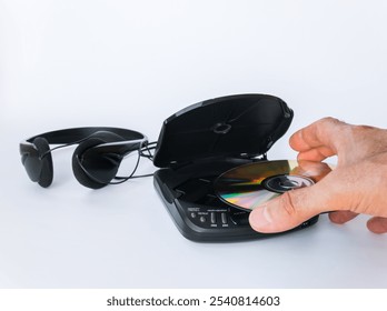 Close up of a man's hand inserting a compact disc into a compact disc player with headphones isolated on white background.