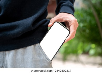 Close up of man's hand pulling out white screen smartphone from pants pocket getting a call while standing outdoor. Advertising Mockup, Online Society.