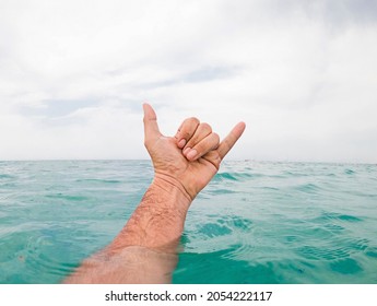 Close up of man's hand showing shaka sign above sea water against sky. Hand of a man coming out of sea water surface and gesturing shaka sign against cloudy sky - Powered by Shutterstock
