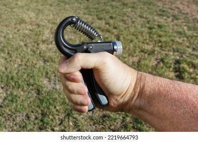 Close Up Of Man's Hand Using An Adjustable Hand Strengthener To Exercise The Forearm And Strengthen The Grip