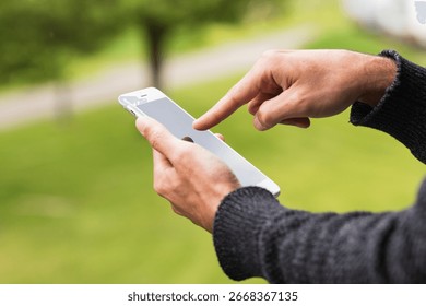 Close up of a man's hand using mobile smart phone outside on sunny summer day