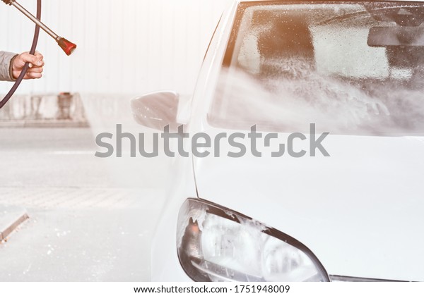 Close up mans hand washing a white\
car using high pressure water. Car self washing service\
