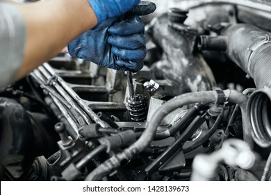 Close up of man's hands in dusty rubber gloves keeping screwdriver and tighten bolts in spark plugs from car engine. Diagnostic, maintenance and reparing in service station