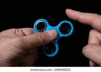 Close up of man's hands holding fidget twist spinner on a black background. closeup. Concept of stress reduction.