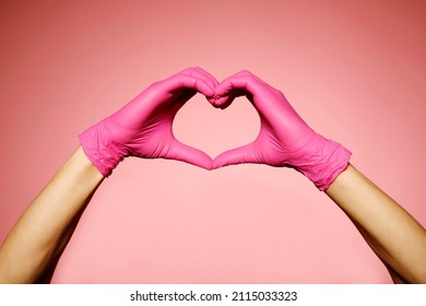 Close up man's hands in pink protective gloves making heart sign with hands over pink background. Valentine's Day, 8th March, anniversary romantic concept. - Shutterstock ID 2115033323