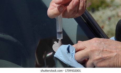 Close Up Of A Man's Hands Repairing Small Impact Hole In Car Windshield With DIY Kit                               