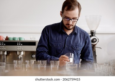 Close Up Of Man's Hands Tasting Freshly Brewed Coffee In Glass Cup, Using Spoon, Examining Coffee Taste And Flavour At Coffee Cupping Test For Barosta