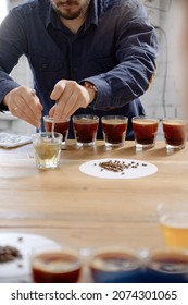 Close Up Of Man's Hands Tasting Freshly Brewed Coffee In Glass Cup, Using Spoon, Examining Coffee Taste And Flavour At Coffee Cupping Test For Barosta