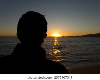 Close up of man's silhouette watching the sunset at sea in winter with the sun setting on the horizon