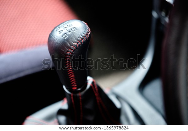 Close up of manual gear shift knob with\
trim black leather & red stitch upholstery. Transmission and\
gearbox concept. Car interior & automotive background. Garage\
& repair service wallpaper.  \
