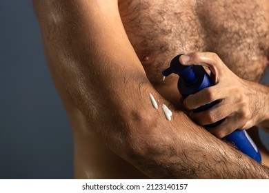 Close Up Of Masculine Man Applying Cream Or Moisturizing Body Lotion Onto Elbows In Bathroom. Selfcare And Wellness Concept