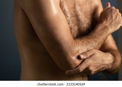 Close Up Of Masculine Man Applying Cream Or Moisturizing Body Lotion Onto Elbows In Bathroom. Selfcare And Wellness Concept