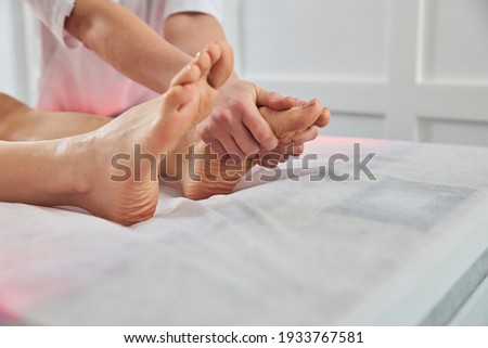 Close up of masseuse hands massaging female foot while lady lying on massage table