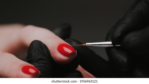 Close Up of master in rubber gloves covering red nails with top coat in the beauty salon. Perfect nails manicure process. Gel polish concept.	