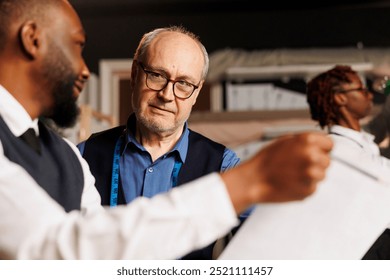 Close up of master tailor teaching skillful craftmanship to aspiring fashion design apprentices in atelier workspace. Diverse team of couturiers working together on bespoken sartorial garments - Powered by Shutterstock