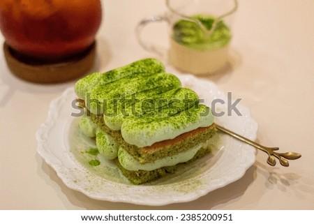 Close up of Matcha cake with sauce matcha, blurred ice tea and small fork served on a table in a dessert cafe. dessert. sweet dish