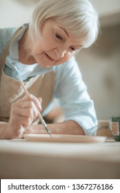 Close Up Of Mature Female Artist Holding Paintbrush And Making Ornament On Earthenware. Concept Of Ceramic Art And Hobby