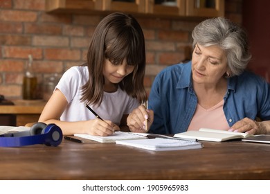 Close Up Mature Grandmother Helping To Granddaughter With School Assignment, Focused Little Girl Writing Notes, Older Teacher Training Pupil, Involved In Lesson At Home, Homeschooling Concept