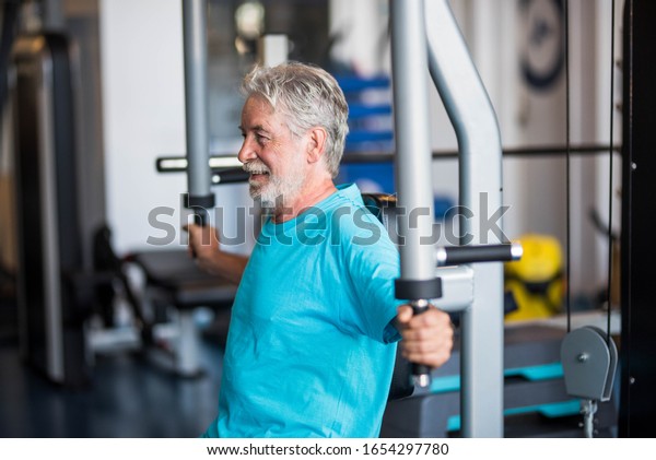 close up of mature man\
at the gym doing exercise alone lifting weight to build his body\
and be fit - active pensioner senior training hard and holding the\
machine of the gym