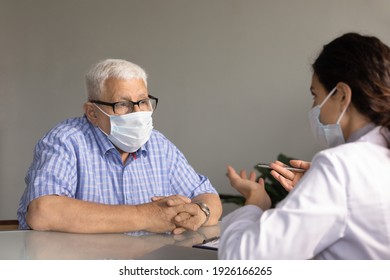 Close Up Mature Man Wearing Glasses And Medical Face Mask Listening To Female Doctor At Meeting, Therapist Physician Consulting Old Patient, Explaining, Discussing Symptoms Or Checkup Results