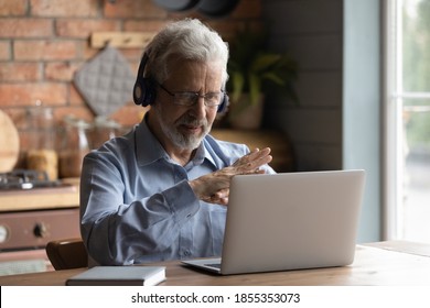Close up mature man wearing headphones using laptop, making video call, sitting at table in kitchen, senior teacher mentor wearing glasses engaged online conference, recording webinar, teaching - Shutterstock ID 1855353073