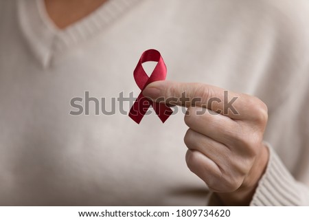 Close up mature woman holding red awareness ribbon in hand, middle aged female supporting people with disease, regular checkup promotion, symbol of fight against AID, HIV, cancer, drugs addiction