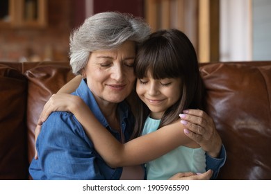 Close up mature woman and little girl hugging with closed eyes, sitting on couch at home, loving older grandmother and adorable granddaughter enjoying tender moment, embracing, two generations - Powered by Shutterstock