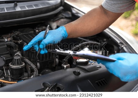 Close up mechanic man with blue rubber gloves checking car problem lists in auto repair garage, car mechanic check up and maintenance openhooded car 