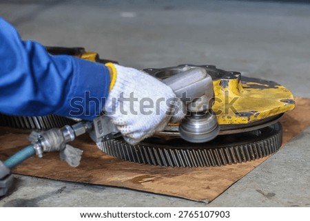 Close up of a mechanic using a pneumatic angle grinder to clean and polish a heavy industrial metal gear in a workshop for maintenance and repair.