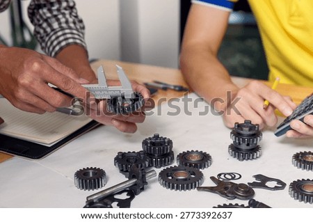 Close up of mechanical engineer hands using vernier caliper to measure metal gear dimension. Two engineers working together on mechanical parts. Industrial machinery design and manufacturing concept.